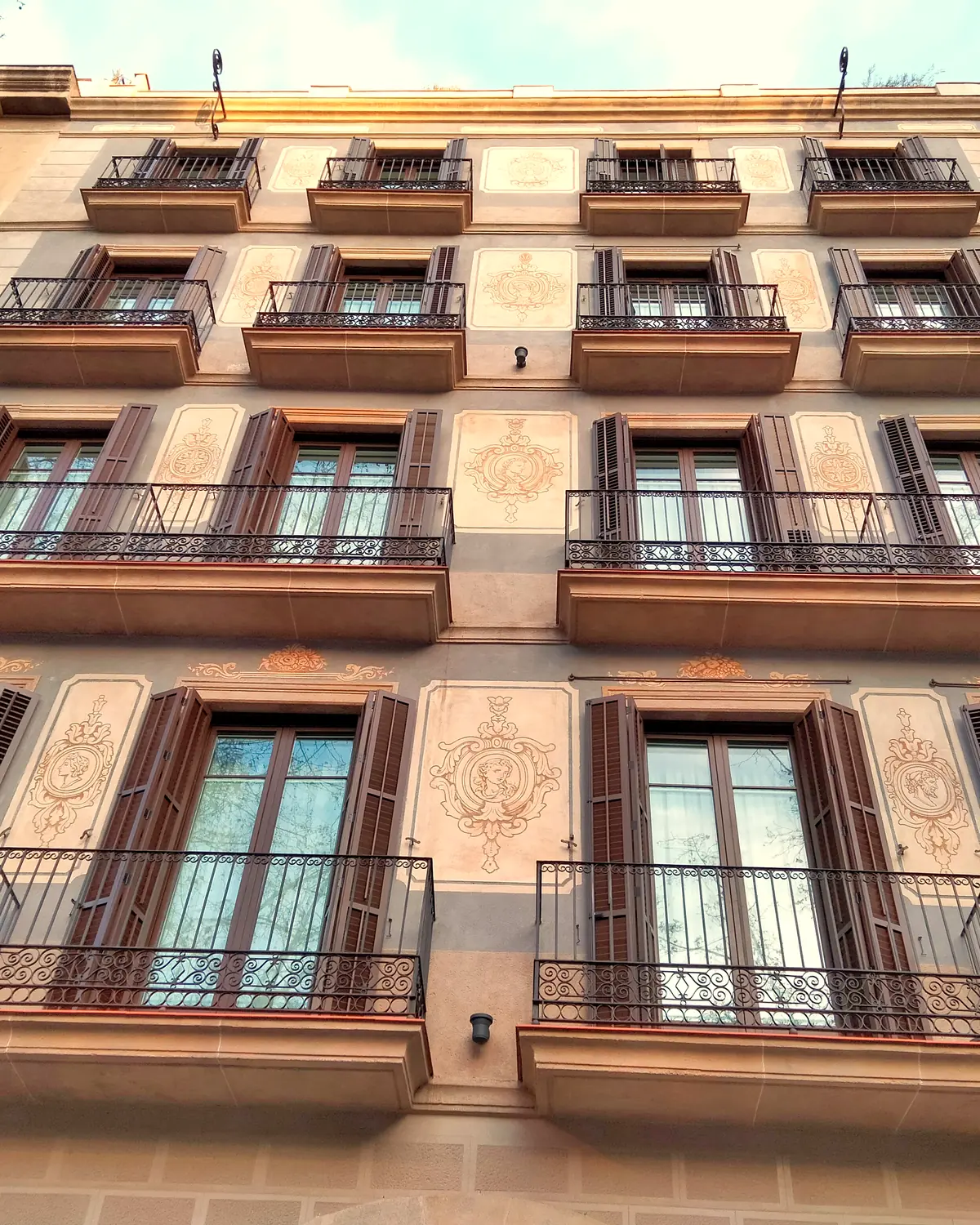 Painted facade of Antiga Casa Buenavista: iron balconies, brown shutters and sgraffito medallions on Ronda de Sant Antoni