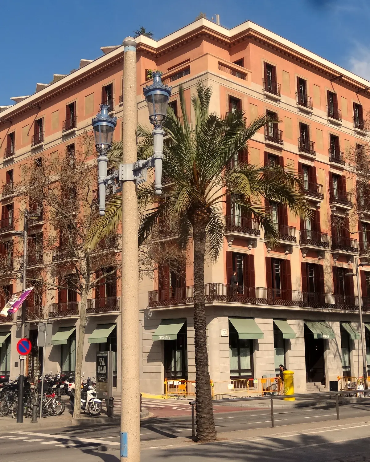 Corner facade of Soho House Barcelona on Plaça del Duc de Medinaceli: salmon walls, dark shutters, green awnings and palm trees