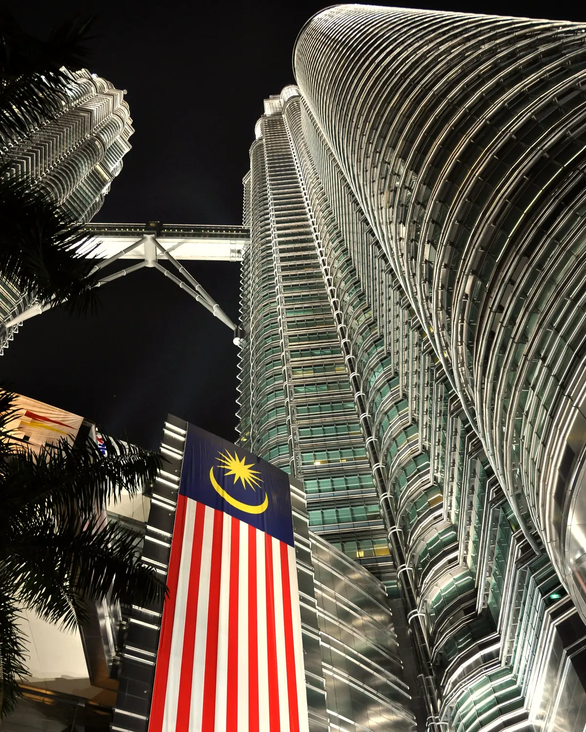 Petronas Towers, Kuala Lumpur, Malaysia. Photo taken at night from the base of one of the towers looking up towards the other tower. One of the large Malaysian flags on one of the 