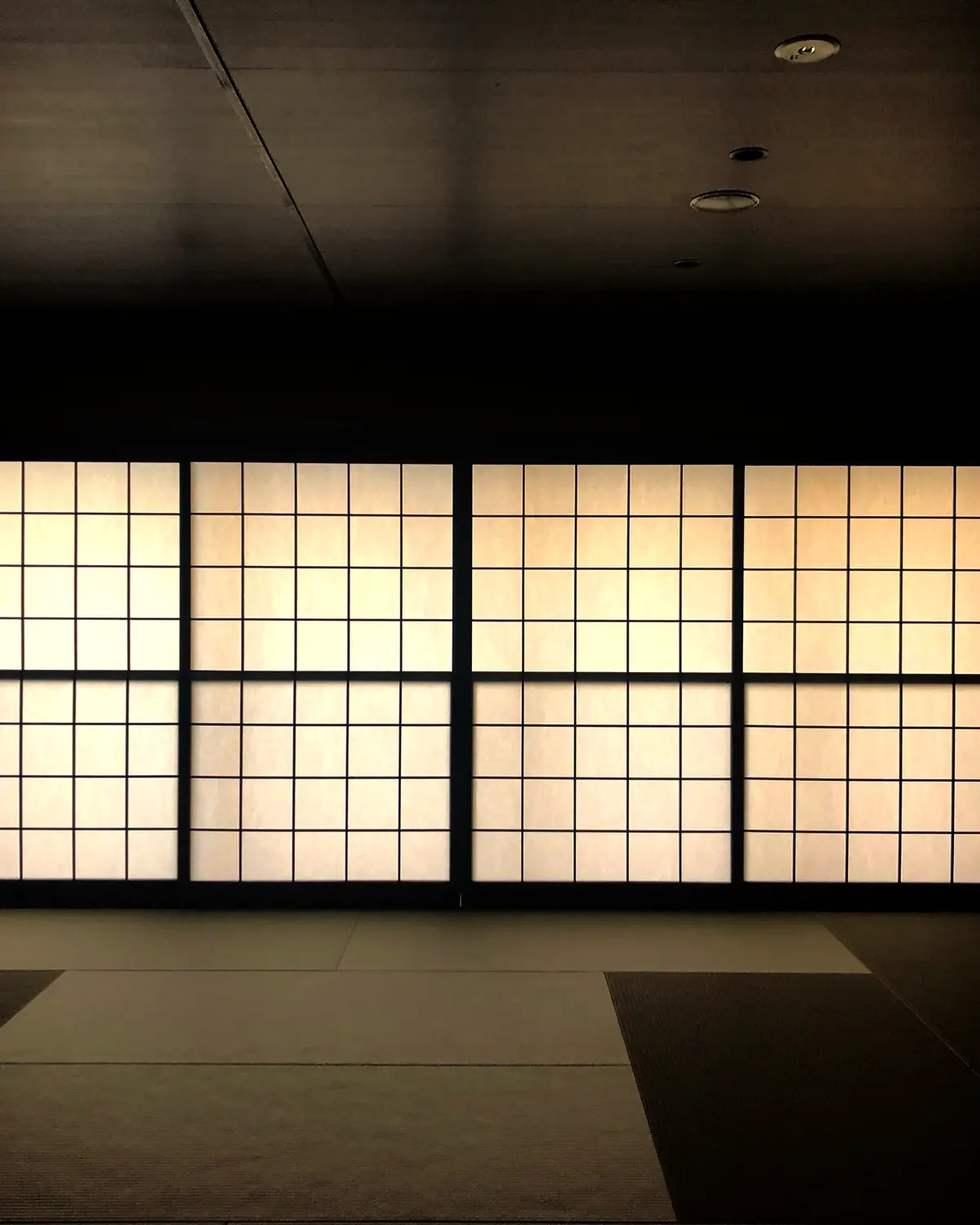 A dark tatami room at ENSO ANGO with a wall of lit shoji screens