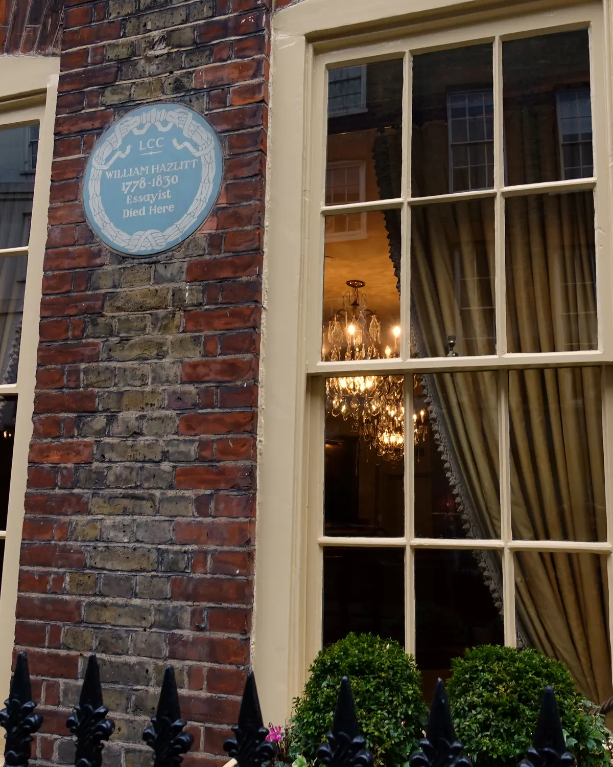 Brick front of Hazlitt's on Frith Street: sash windows, the William Hazlitt blue plaque, and a chandelier seen through the glass