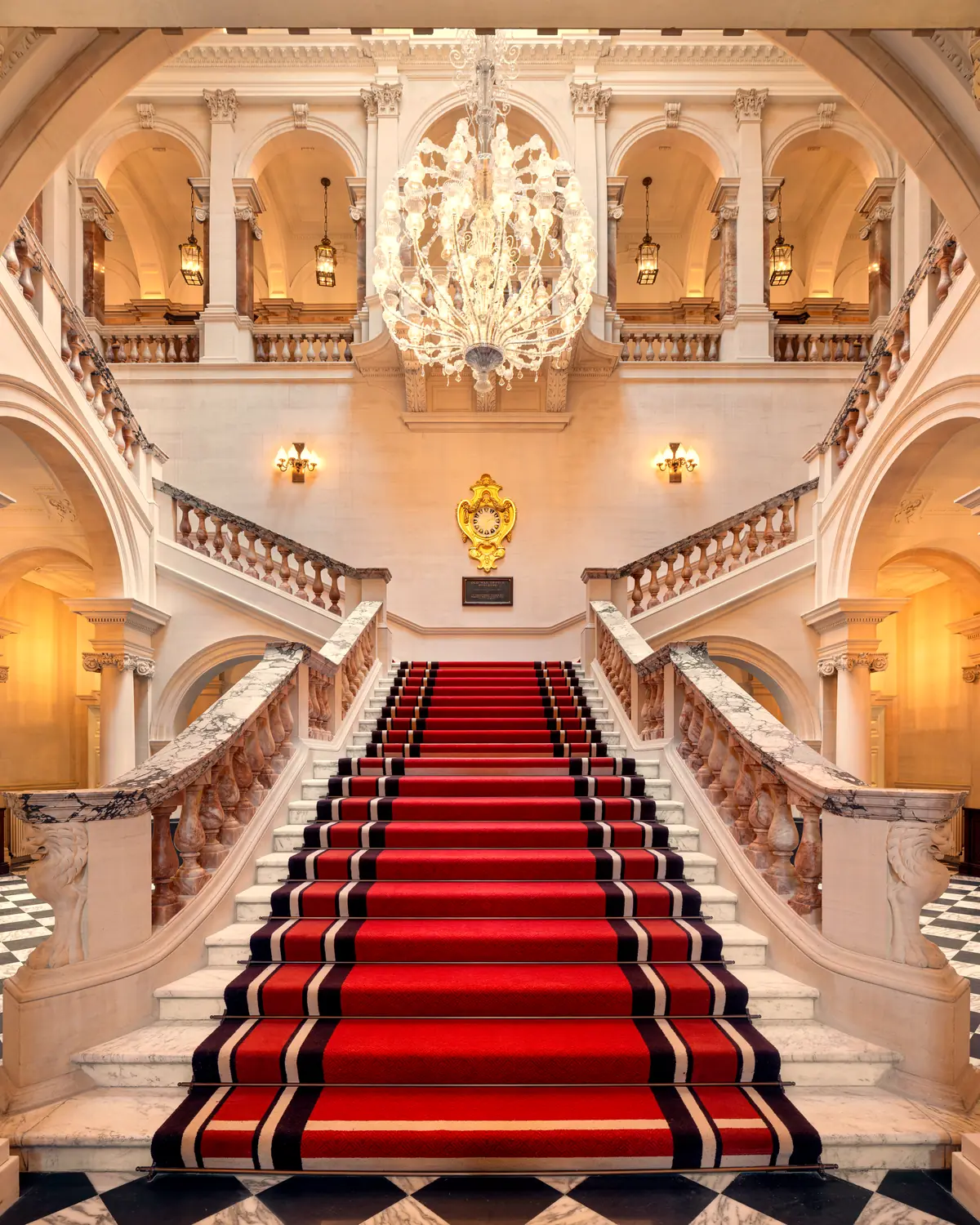 The grand marble staircase with red runner and chandelier (gallery caption: 'Raffles London at the OWO')