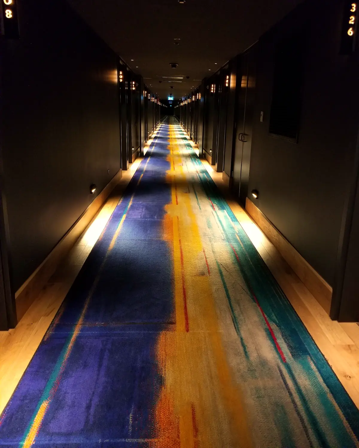 A guest-floor corridor at QT Melbourne: a painted runner between dark doors, with room numbers 308 and 326