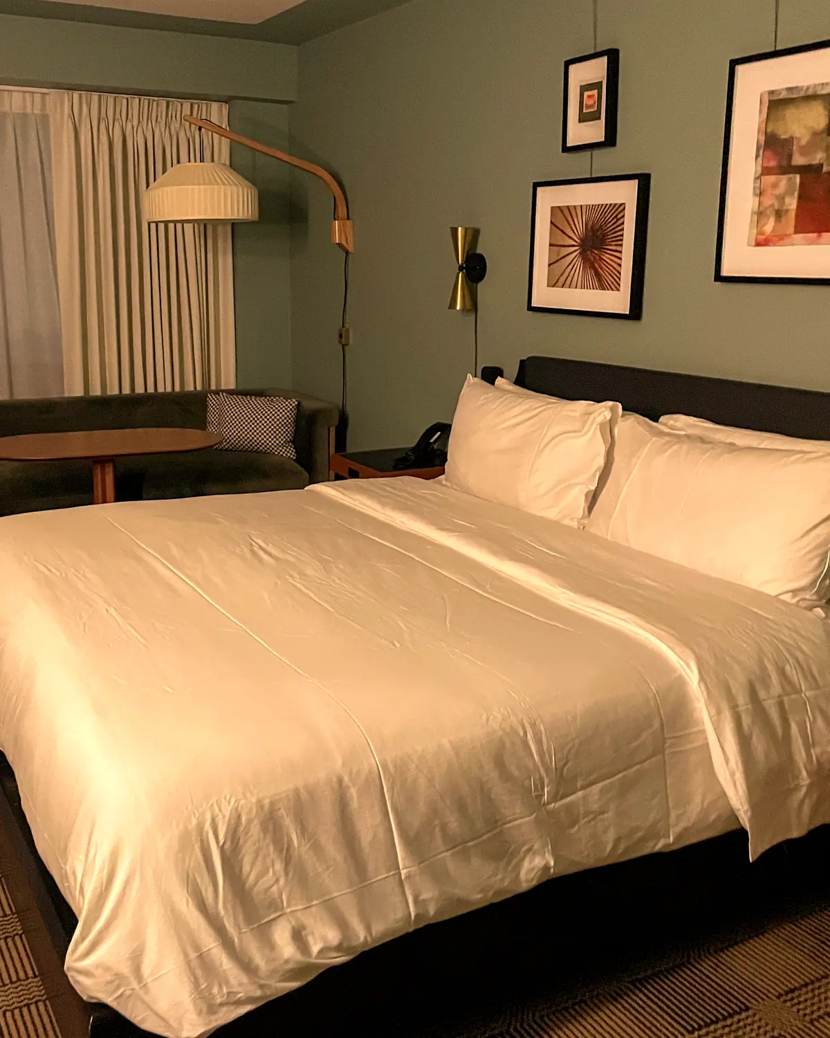 A guest room at Romer Hell's Kitchen: a made bed, a green sofa by the window and framed prints on a teal wall