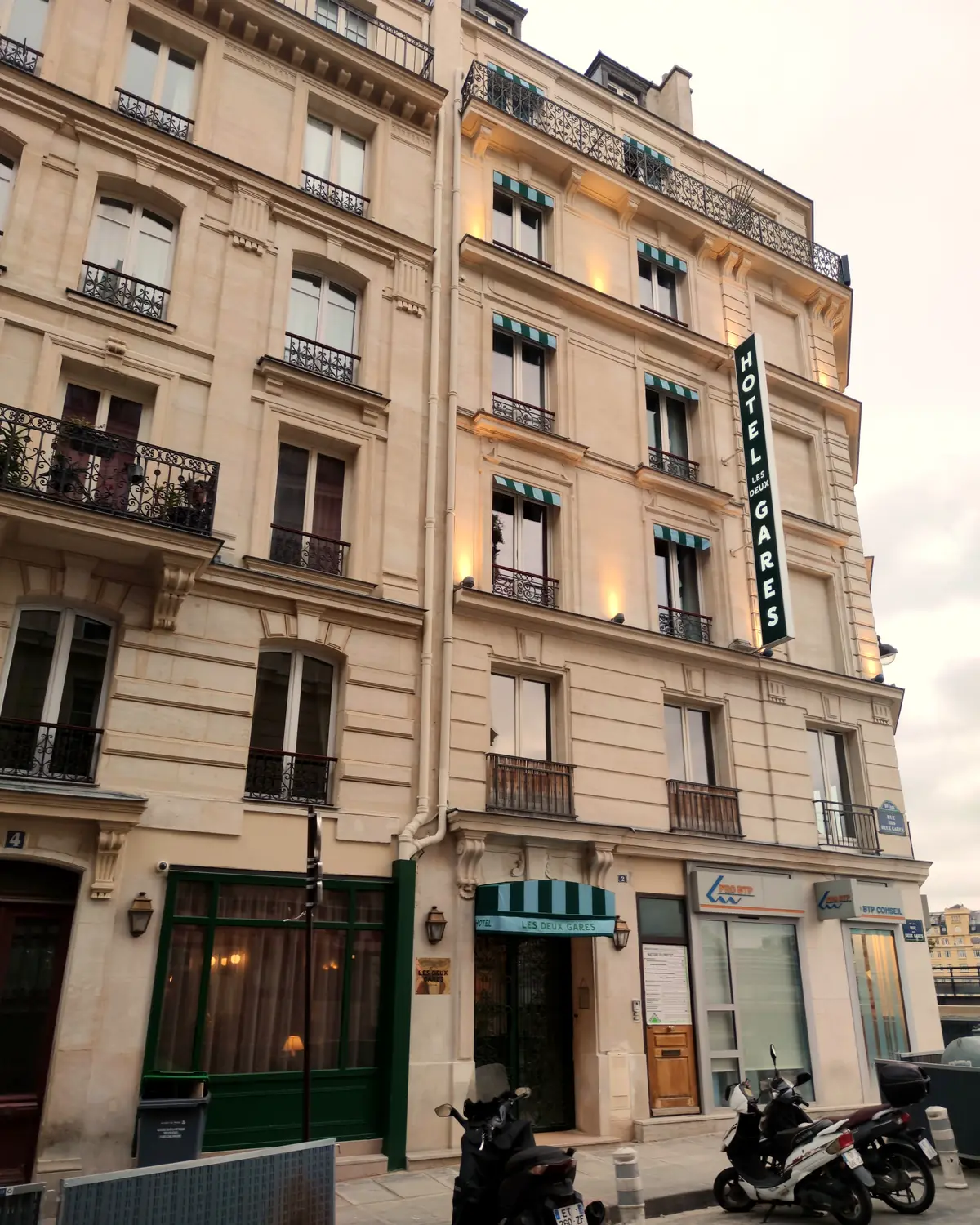 Haussmann facade of Hôtel Les Deux Gares on rue des Deux-Gares, with green awnings and a vertical hotel sign