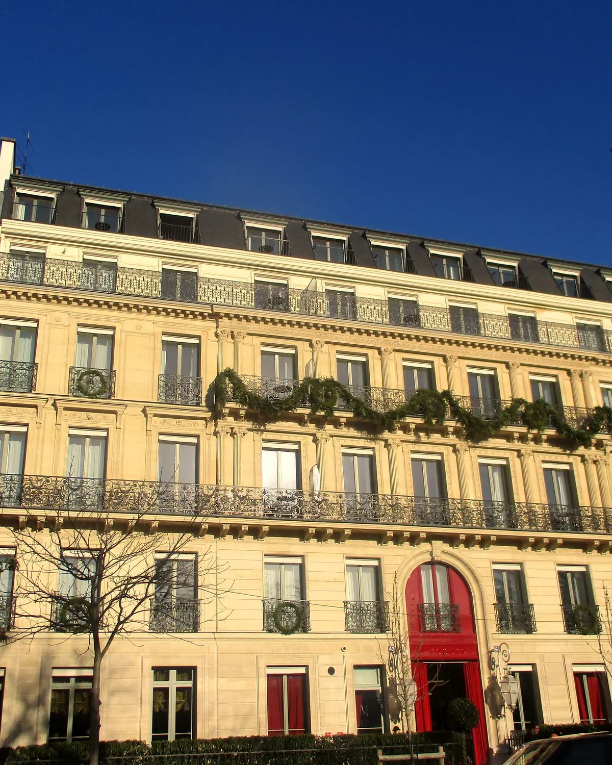 Exterior: the hotel's facade at 42 avenue Gabriel, with the red arched entrance door and wreaths on the balconies. La Réserve Paris Hotel & Spa