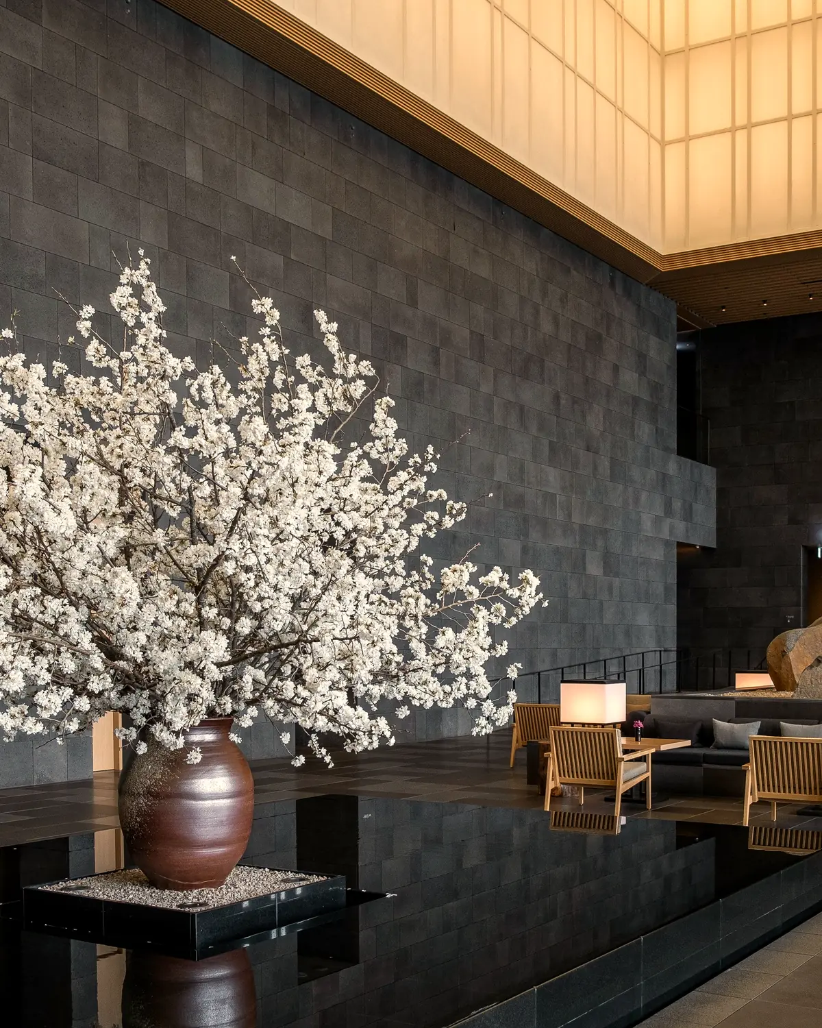 The lobby lounge: dark stone walls, a lit washi-paper ceiling, a stone garden, and a cherry-blossom centrepiece in a vase