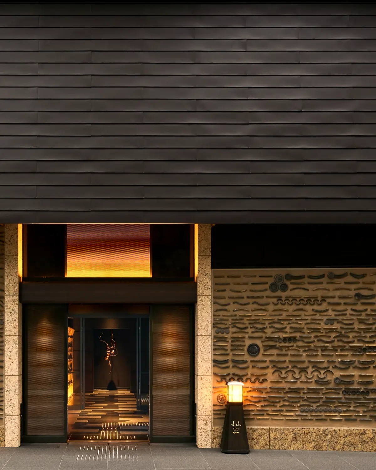 The entrance of FUFU Tokyo Ginza: a tiled canopy, a carved stone wall, and a lantern