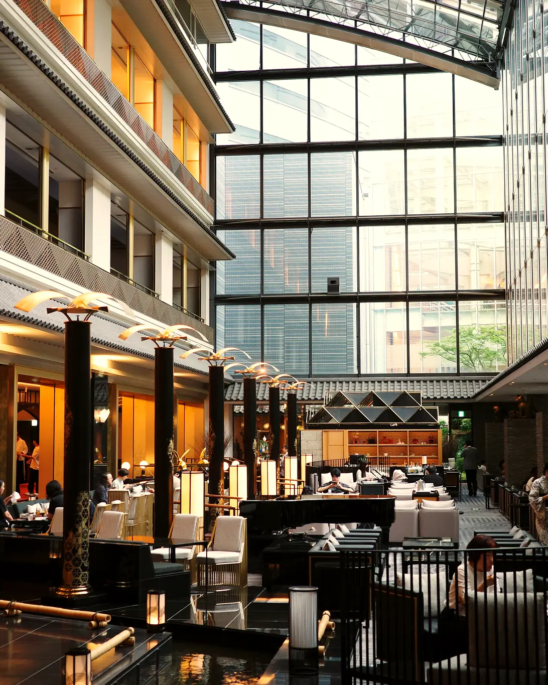 Glass-walled atrium with lounge/cafe seating, black lantern columns and tiled eaves. Gajoen Tokyo