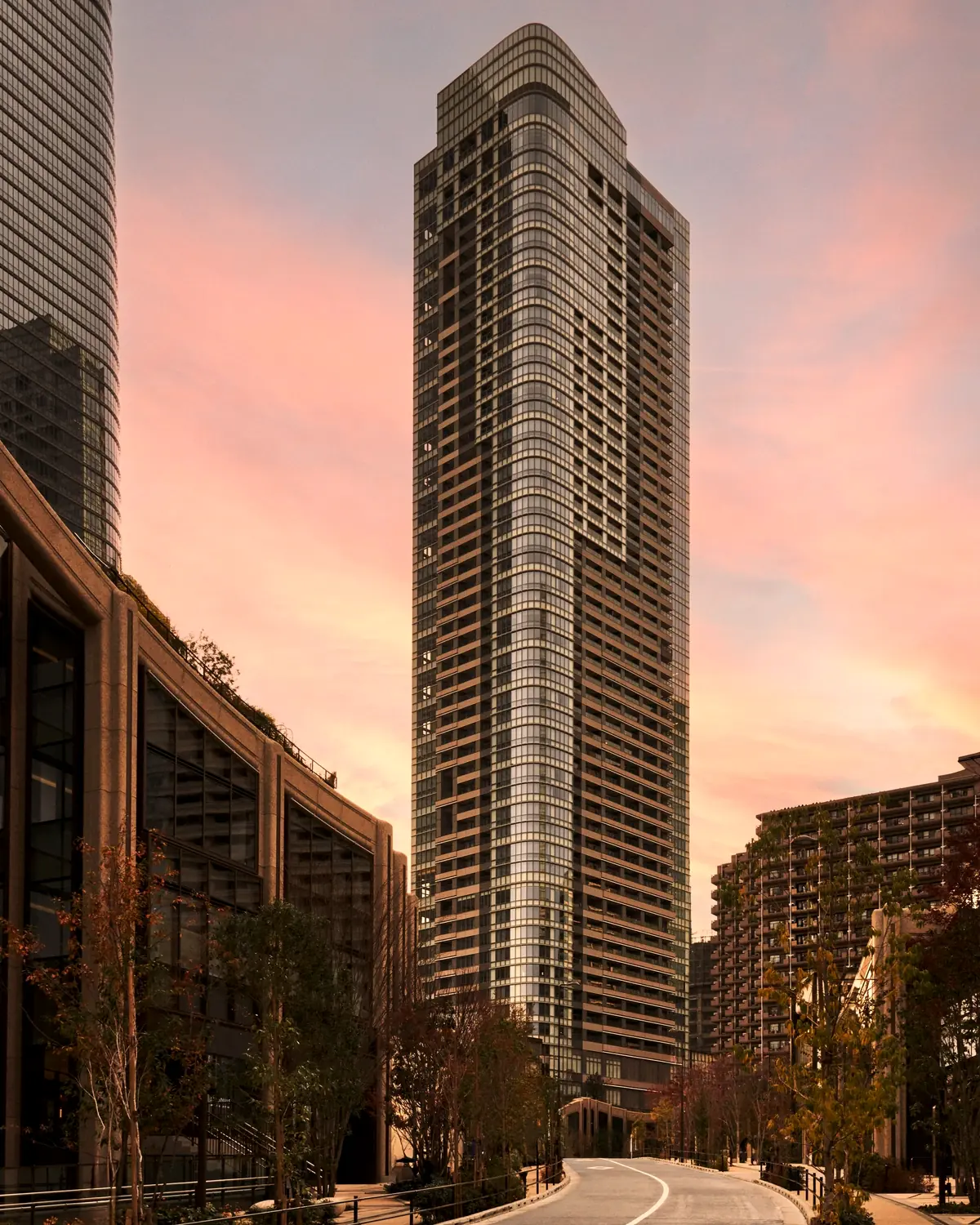 Exterior image from the opening release: a residential-style tower at Azabudai Hills at dusk, with a low stone building and street trees in front